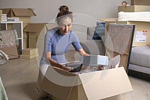 Asian woman moving into new house holding and unpacking her belongings with cardboard boxes