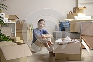 Asian woman moving to new home sitting on floor smiling and looking at camera