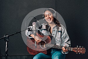 Asian woman in music studio recording with guitar