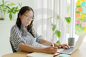 Asian woman noting down important information working at home, Asia businesswomen using computer laptop at home office, Side view