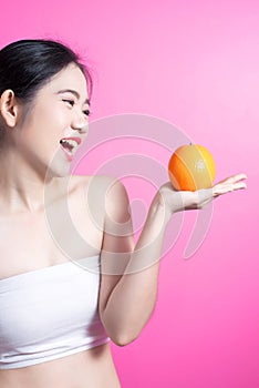 Asian woman with orange concept. She smiling and holding orange. Beauty face and natural makeup. Isolated over pink background.