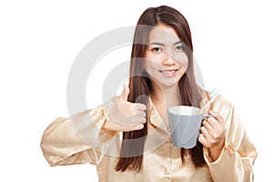 Asian woman in pajamas thumbs up with toothbrush in mug