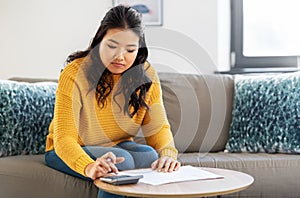 Asian woman with papers and calculator at home