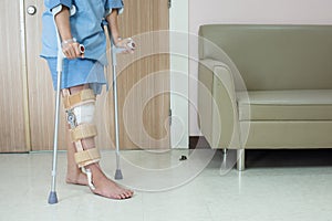 Asian woman patient with knee brace with walking stick and knee braces support in hospital ward after ligament surgery