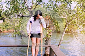 Asian woman patient using crutch and broken leg for walking at nature