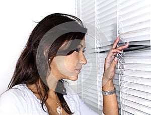 Asian woman peering through white shades