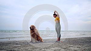 Asian woman performs yoga stretching exercises with dog at the beach. Golden Retriever lifestyle on summer holiday