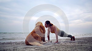 Asian woman performs yoga stretching exercises with dog at the beach. Golden Retriever lifestyle on summer holiday