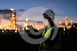 Asian woman petrochemical engineer working at night with digital tablet Inside oil and gas refinery plant industry factory at