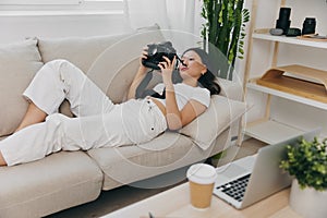 Asian woman photographer lying at home on couch and looking at photos in camera, freelance photographer business for