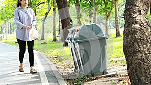 Asian woman picking up litter from the floor into the trash can,female people picking up garbage plastic bag on the grass at park,