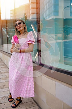 Asian woman in a pink dress and sunglasses with an umbrella is sitting in the center of the city