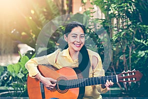 Asian woman playing acoustic guitar with bright sunlight. Vinta