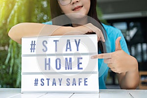 Asian woman pointing a lightbox sign with text hashtag  STAY HOME and  STAY SAFE. COVID-19. Stay home save concept