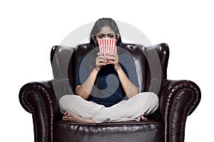 Asian woman with popcorn sitting on the couch with a scared expression