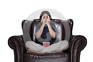 Asian woman with popcorn sitting on the couch with a scared expression