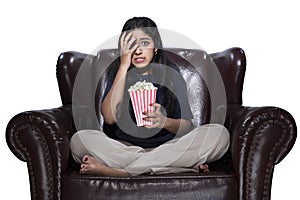 Asian woman with popcorn sitting on the couch with a scared expression