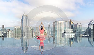 Asian woman pose yoga action on hotel rooftop with Bangkok city and swimming pool background