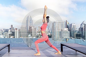 Asian woman pose yoga action on hotel rooftop with Bangkok city and swimming pool background