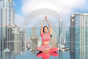 Asian woman pose yoga action on hotel rooftop with Bangkok city and swimming pool background