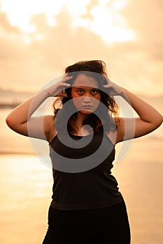 an Asian woman posing with her hands raised and touching her black hair passionately on the beach