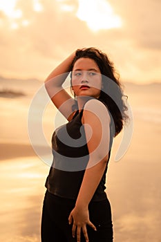 an Asian woman posing with her hands raised and touching her black hair passionately on the beach