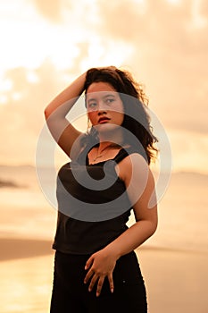 an Asian woman posing with her hands raised and touching her black hair passionately on the beach