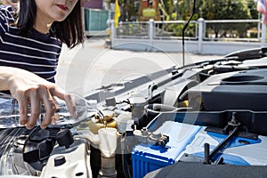 Asian woman pouring clean water from bottle into the windshield washer fluid tank of a car,female filling the windshield washer