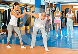 Asian woman practicing painful wristlock on male opponent in gym