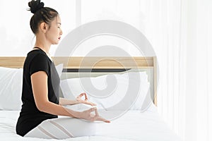 Asian woman practicing yoga, doing Half Lotus pose with mudra gesture on bed in the bedroom