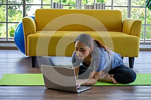 Asian woman practicing yoga  exercise at begining level from online lesson playing on laptop computer