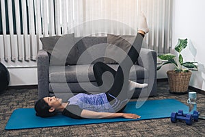 Asian woman practicing yoga at home while lying on a mat and stretching her legs