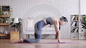 Asian woman practicing yoga pose Cat and Cow at home