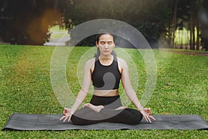 Asian woman practicing yoga in Root Bond, Mula Bandha pose on the mat in outdoor park photo