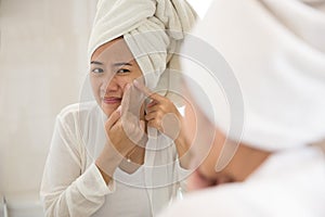 Asian woman pressing acne on her cheek