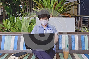 Asian woman in protective mask using laptop computer on vintage wooden bench in rest area inside of shopping mall