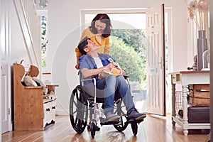 Asian Woman Pushing Husband In Wheelchair At Home Back From Shopping Trip With Bag
