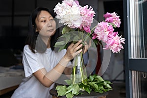 Asian woman puts peonies flowers in vase. Sweet home. Allergy free.