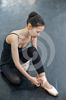 Asian woman puts on pointe shoes by tying ribbons on her ankle.