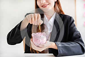 Asian woman putting coin into piggy bank. Saving money with coins Step into a business that is growing to be successful and save