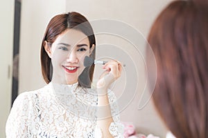 Asian woman putting makeup in home using a contour brush to apply blonze powder under cheek bones make-up mirror.