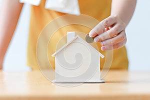 Asian woman putting money coin in to house piggy bank metaphor s