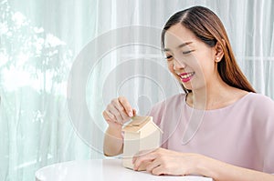 Asian woman putting money coin in to house piggy bank metaphor saving money financial for buy the home