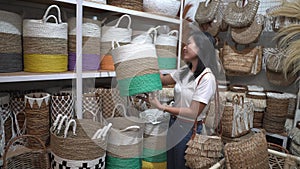 Asian woman raises wicker baskets standing among the handicraft items