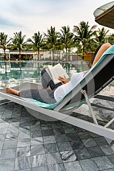 Asian woman reading good book at swimming pool on vacation