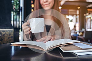 An asian woman reading and opening a book while drinking coffee in cafe