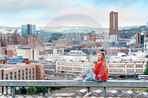 asian woman in a red jacket sitting in front of the city Sheffield and take photos on great summer day