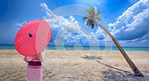 Asian woman in red pink silk dress and red umbrella and with beautiful sea view and blue sky, Coconut trees on the beach with a
