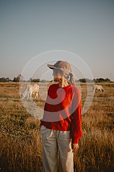 Asian woman in red sweater stands on the grass field with cows and cattle at sunset for the sightseeing.