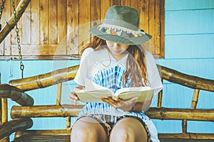 Asian women relax in the holiday. sit read a book on a wooden swing. Home Front porch. In Thailand